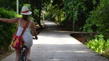 Amanda anda de bicicleta e indica com o braço que vai pegar a rua da esquerda, no cruzamento a sua frente.