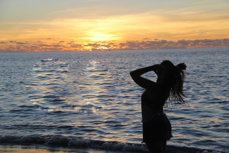 Com luzes do entardecer, Amanda aparece de frente para o mar, enquanto agita os cabelos para curtir a brisa da praia.