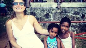 Amanda sorri sentada ao lado de duas crianças que vivem em Seychelles.