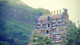 Um dos templos religiosos de Seychelles, com fachada colorida, repleta de estátuas típicas, e cercada por árvores, com uma montanha ao fundo.