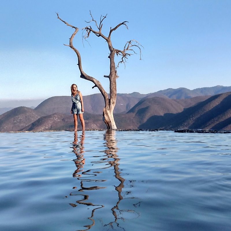 Amanda Noventa em pé na borda da piscina, com paisagem típica de Oaxaca, no México, ao fudo.