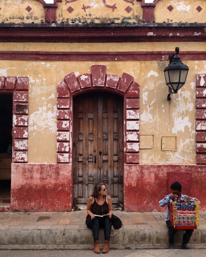 Amanda Noventa sentada em frente a um prédio antigo da cidade de San Cristóbal de las Casas, no México.