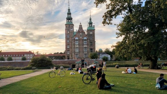 Pessoas curtindo o entardecer no gramado em frente ao Castelo Rosenborg, em Copenhagen, Dinamarca.