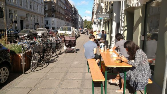 Rua Jægersborggade cercada por prédios antigos e calçadas com estacionamento para bicicletas e mesas de cafés, em Copenhagen, Dinamarca.
