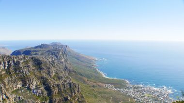 Vista do topo da montanha Table Mountain, em Cape Touwn, África do Sul, mostrando o gradiente entre vegetação verde da montanha e o azul do mar com o do céu.
