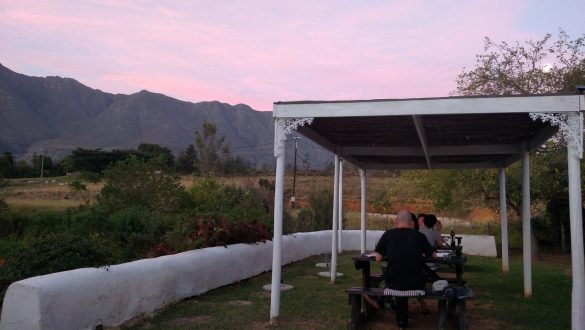 Mesas ao ar livre, com tenda coberta, e montanha ao fundo, no Drostdy Restaurant, na Garden Route, África do Sul.
