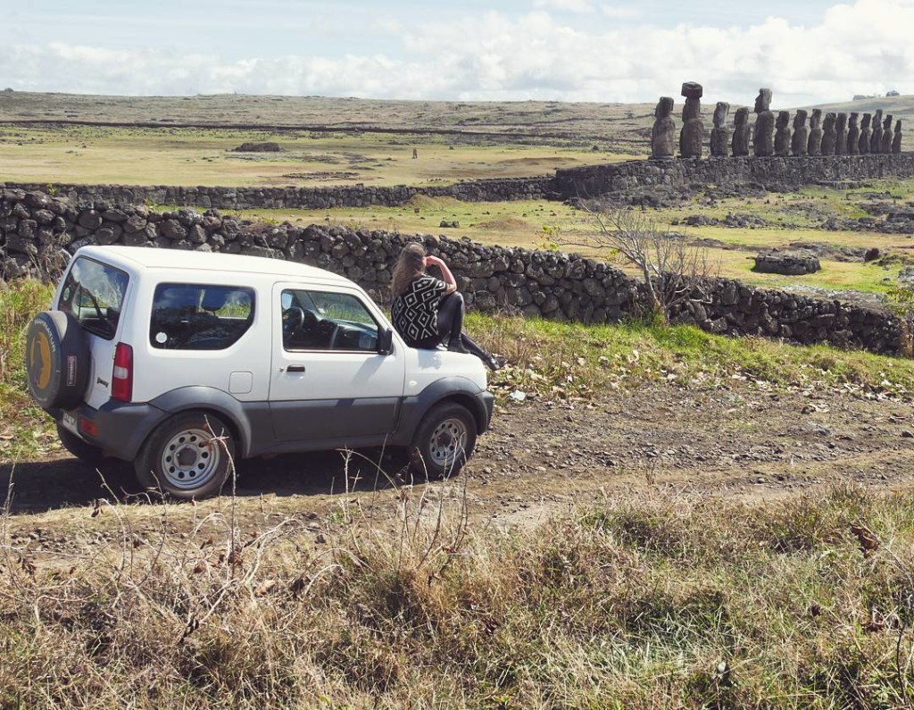 Amanda Noventa, sentada no capô do carro, admira uma das tracionais fileiras de estátuas moais, na Ilha de Páscoa, no Chile.