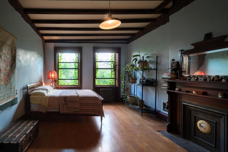 Quarto de hotel em estilo antigo, decorado com plantas e livros, no Harlem Flophouse, hotel em Nova York.