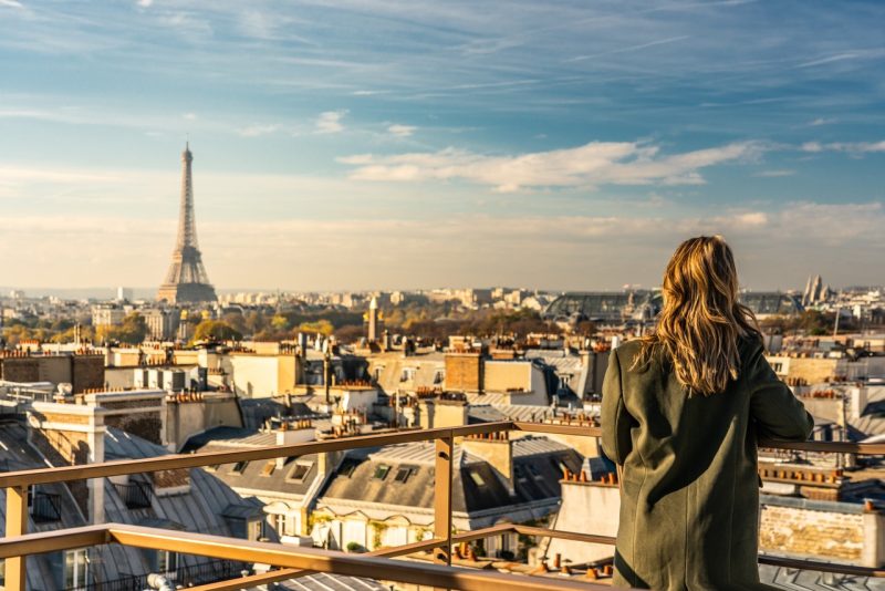 No terraço, Amanda observa a cidade de Paris, com a torre Eiffel ao fundo.