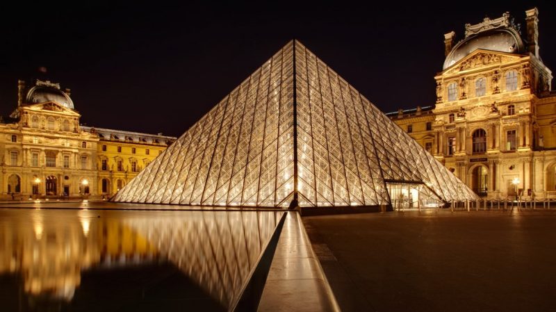 Pirâmide cartão postal em frente ao Louvre, em Paris, com iluminação noturna.